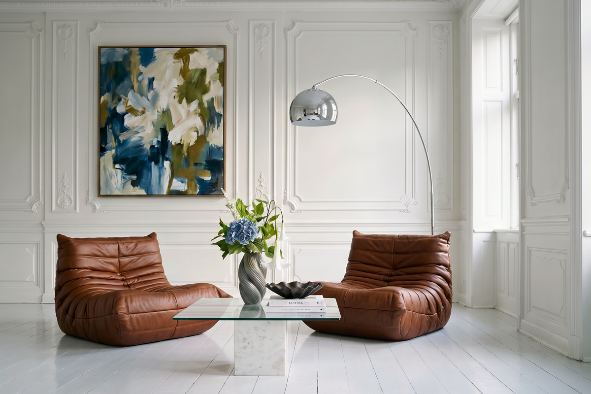Bloomgaard stylet stue i en klassisk københavnerlejlighed med to cognacfarvede læderloungestole, sofabord i glas og marmor, gulvlampe i krom og en kunstig Bloomgaard-buket med blå hortensia og hvide engletrompeter i en skulpturel vase