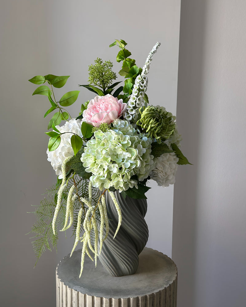 Blush Arbour buket fra Bloomgaard med lyserød pæon, hortensiaer og hvid amarant i grågrøn vase på en piedestal