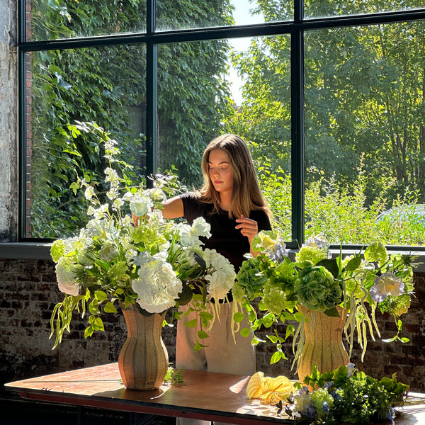 Store hvide og groenne kunstige blomsterbuketter arrangeres på et bord i Lokomotivværkstedet i København