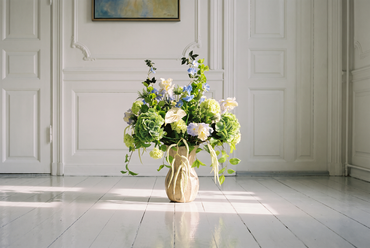Bloomgaard stylet stue i en klassisk københavnerlejlighed med to cognacfarvede læderloungestole, sofabord i glas og marmor, gulvlampe i krom og en kunstig Bloomgaard-buket med blå hortensia og hvide engletrompeter i en skulpturel vase
