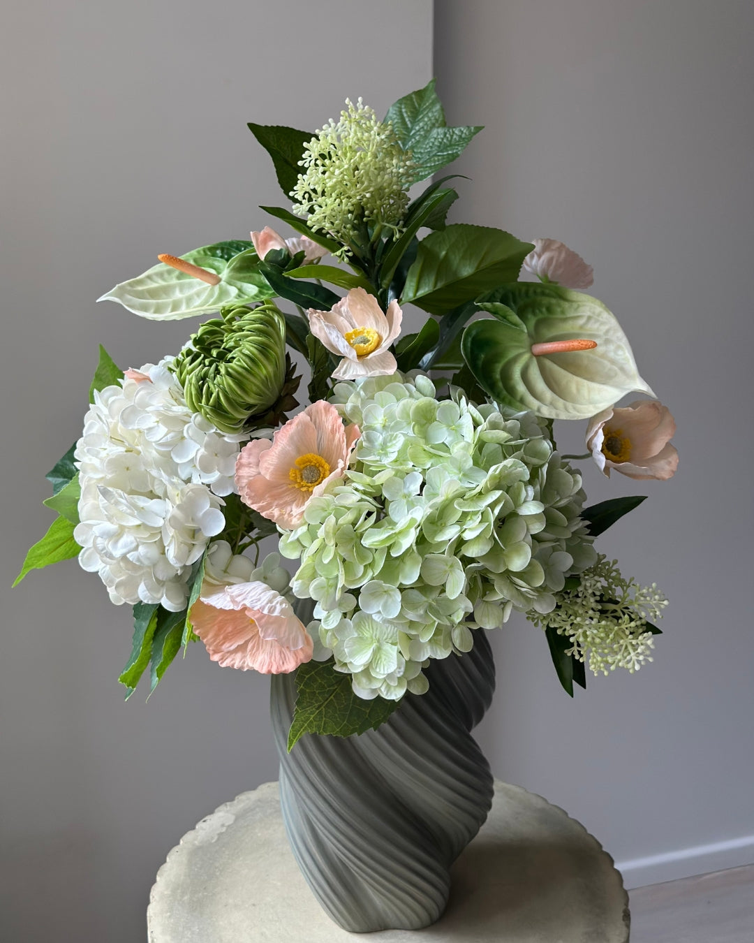 Blush Pavilion artificial bouquet with white and green hydrangeas, peach poppies, green anthurium and a green cactus dahlia bud in a grey-green twisted vase
