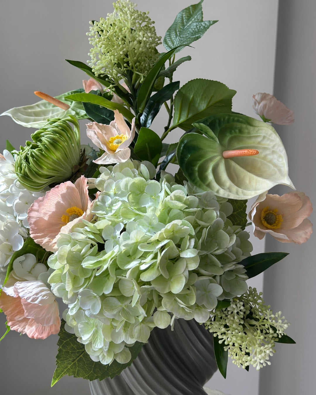 Blush Pavilion artificial bouquet with white and green hydrangeas, peach poppies, green anthurium and a green cactus dahlia bud in a grey-green twisted vase