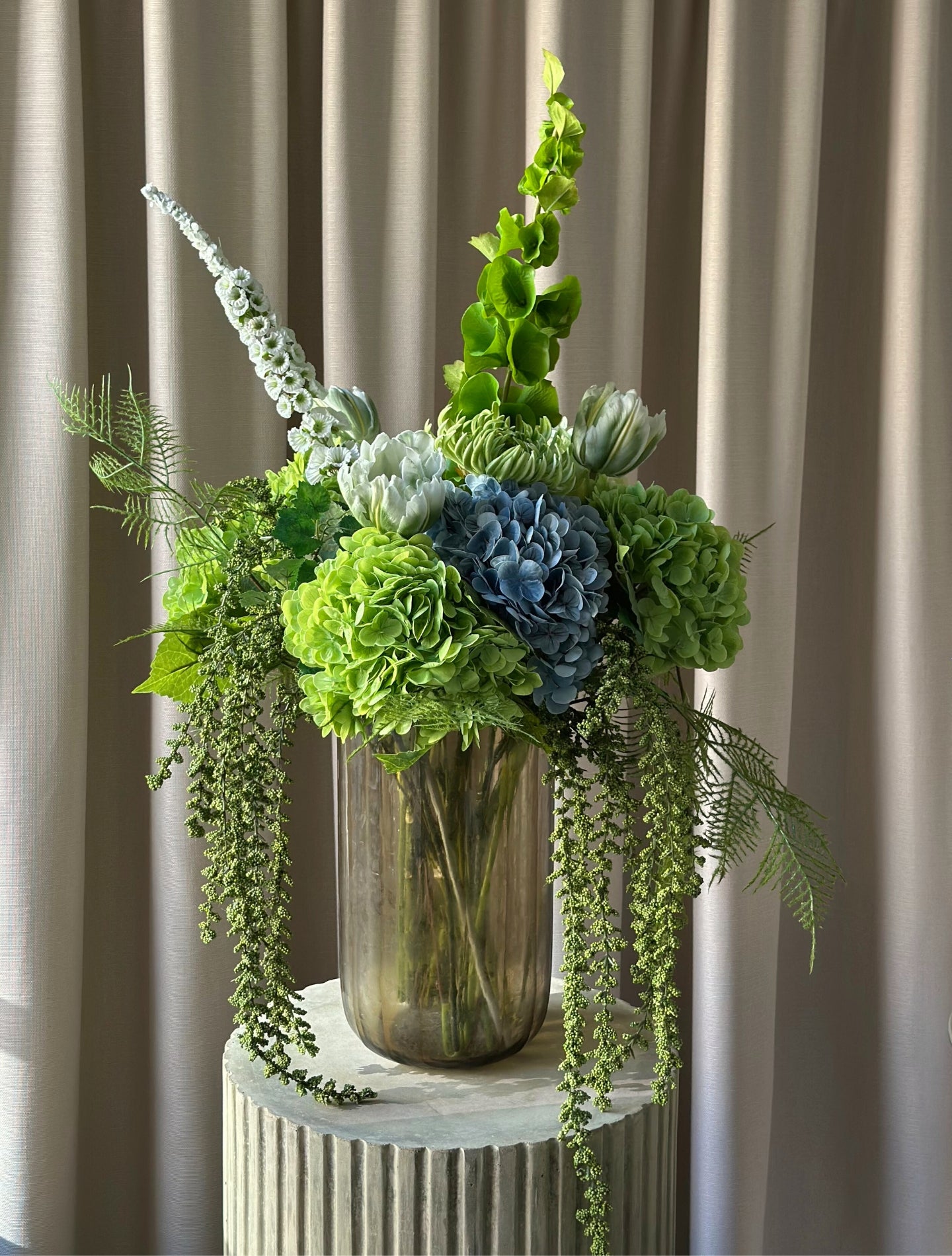 En stor, imponerende buket, hvor grønne nuancer smelter sammen med kølige blå toner i en elegant og luksuriøs komposition. Buketten emmer af eksklusivitet, ro og styrke – ideel som centerpiece eller som en markant, betagende dekoration i hjemmet eller på kontoret.

Buketten er bygget op af store, silkebløde hortensiahoveder i grøn og blå, omgivet af elegante tulipaner, chrysanthemum og karakterfulde foxtail og bells of ireland, der tilfører buketten en skulpturel lethed, mens de luftige bregner og hængende 