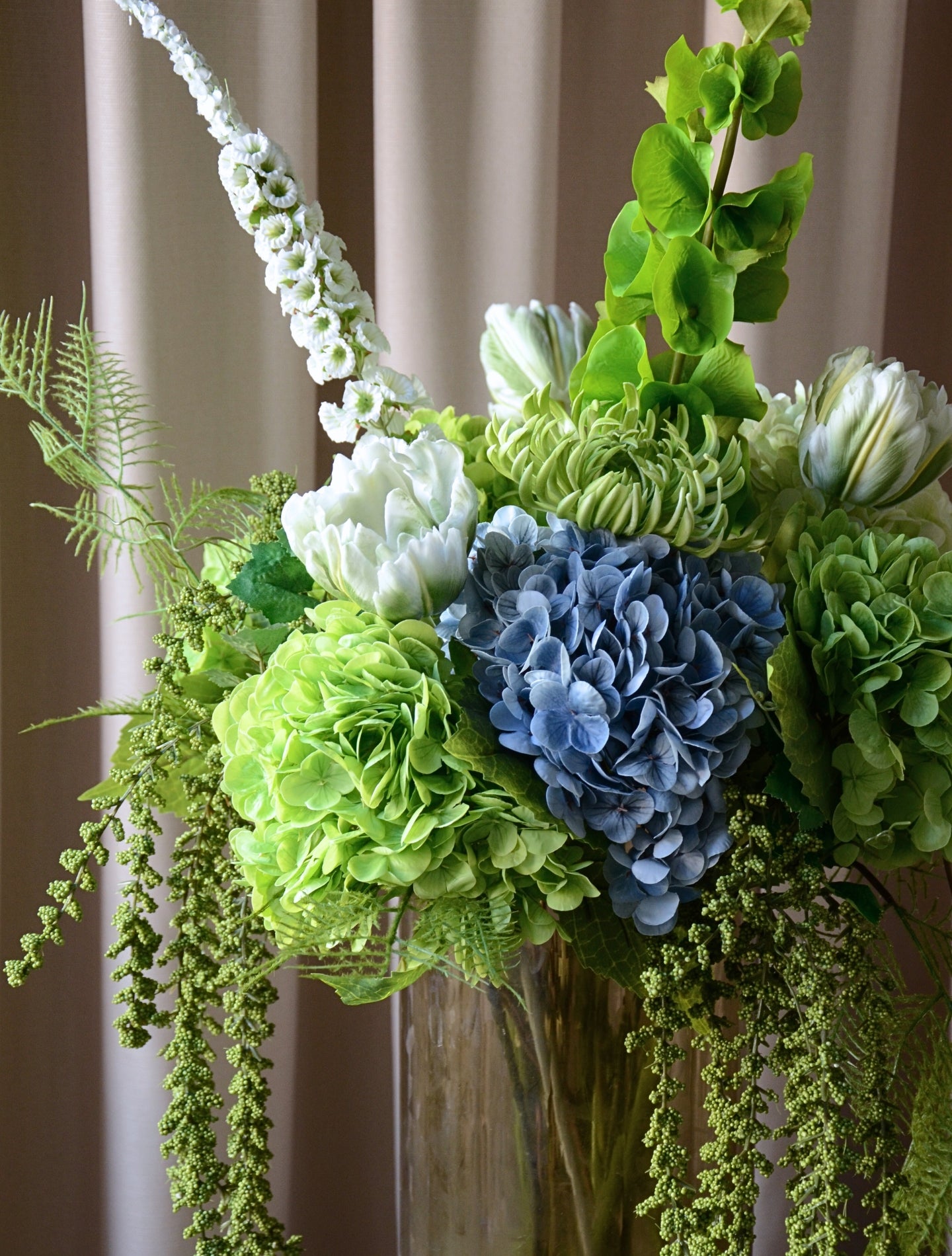 En stor, imponerende buket, hvor grønne nuancer smelter sammen med kølige blå toner i en elegant og luksuriøs komposition. Buketten emmer af eksklusivitet, ro og styrke – ideel som centerpiece eller som en markant, betagende dekoration i hjemmet eller på kontoret.

Buketten er bygget op af store, silkebløde hortensiahoveder i grøn og blå, omgivet af elegante tulipaner, chrysanthemum og karakterfulde foxtail og bells of ireland, der tilfører buketten en skulpturel lethed, mens de luftige bregner og hængende 