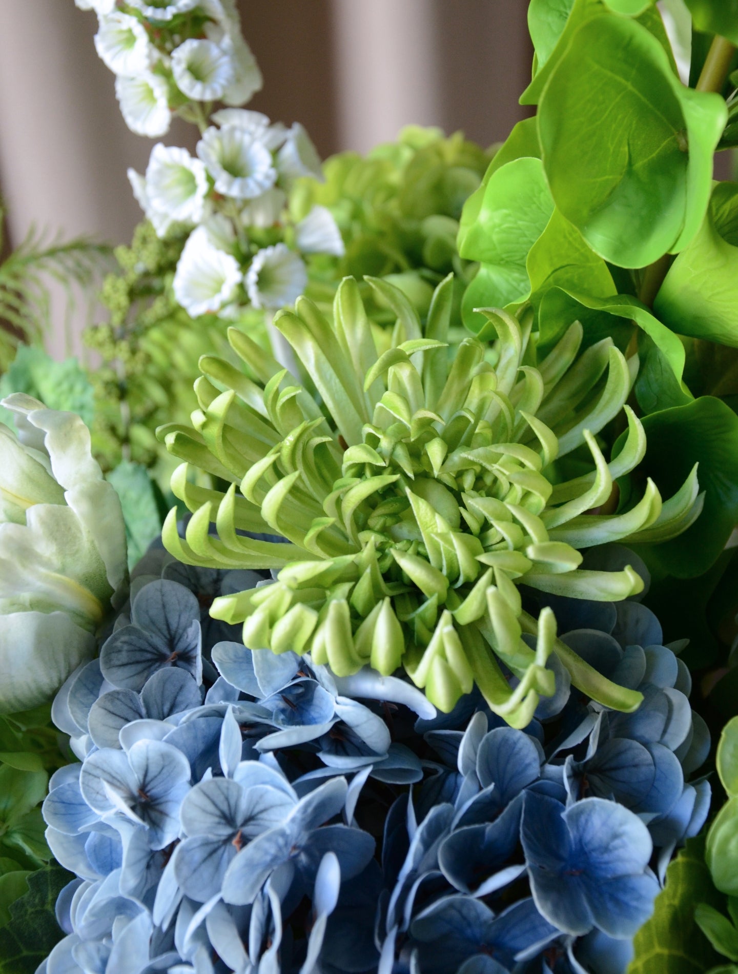 En stor, imponerende buket, hvor grønne nuancer smelter sammen med kølige blå toner i en elegant og luksuriøs komposition. Buketten emmer af eksklusivitet, ro og styrke – ideel som centerpiece eller som en markant, betagende dekoration i hjemmet eller på kontoret.

Buketten er bygget op af store, silkebløde hortensiahoveder i grøn og blå, omgivet af elegante tulipaner, chrysanthemum og karakterfulde foxtail og bells of ireland, der tilfører buketten en skulpturel lethed, mens de luftige bregner og hængende 