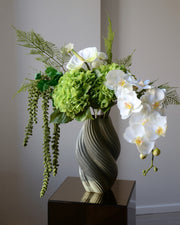 En elegant evighedsbuket i klare hvide og grønne nuancer, hvor den smukke orkidé får lov at træde i karakter med sit yndefulde udtryk. De fine, silkebløde kronblade er udformet med stor omhu og føles næsten som en ægte blomst. Kombinationen af lyse toner og friske grønne elementer skaber et roligt, sofistikeret udtryk – perfekt til dig, der elsker et let og eksklusivt look i hjemmet.
Både tidløs og moderne på én gang.