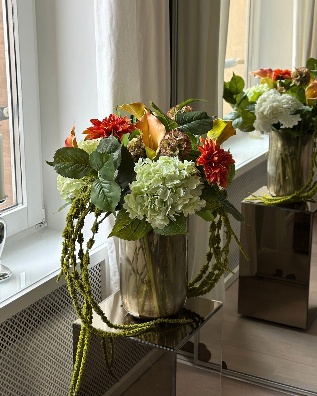 Golden Ember er en storslået og varm kunstig buket, der stråler af dybe, gyldne efterårs nuancer. Den imponerende sammensætning af fyldige grønne og hvide Hortensiaer, glødende orange Dahliaer, elegante Calla Liljer, brunlige Skabioser, Rævehaler og dekorative grene skaber en dramatisk og luksuriøs helhed. Farvepaletten balancerer varme jordtoner med bløde, neutrale nuancer, hvilket giver buketten et rigt og harmonisk udtryk.

Golden Ember er perfekt til at tilføre hjemmet en følelse af varme og raffinement