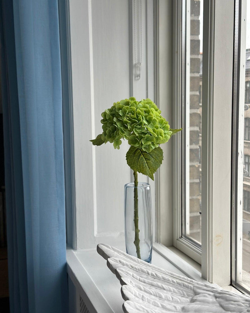 Grøn kunstig hortensia i en vase placeret i vindueskarm