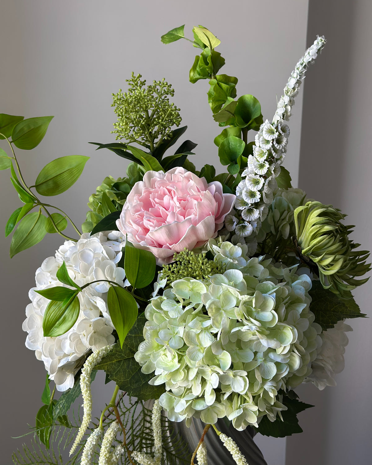 Blush Arbour buket fra Bloomgaard med lyserød pæon, hortensiaer og hvid amarant i grågrøn vase på en piedestal