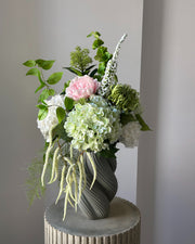 Blush Arbour buket fra Bloomgaard med lyserød pæon, hortensiaer og hvid amarant i grågrøn vase på en piedestal