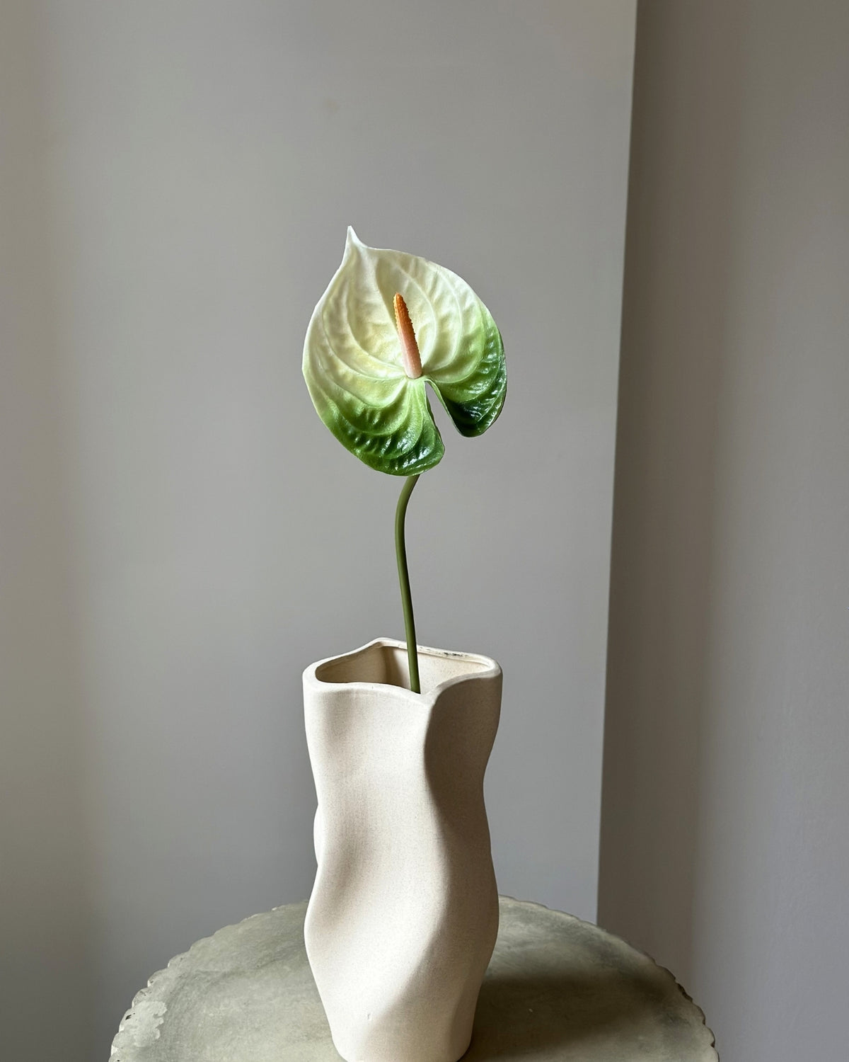 Hvid og groen kunstig anthurium blomsterstilk i en sandfarvet vase