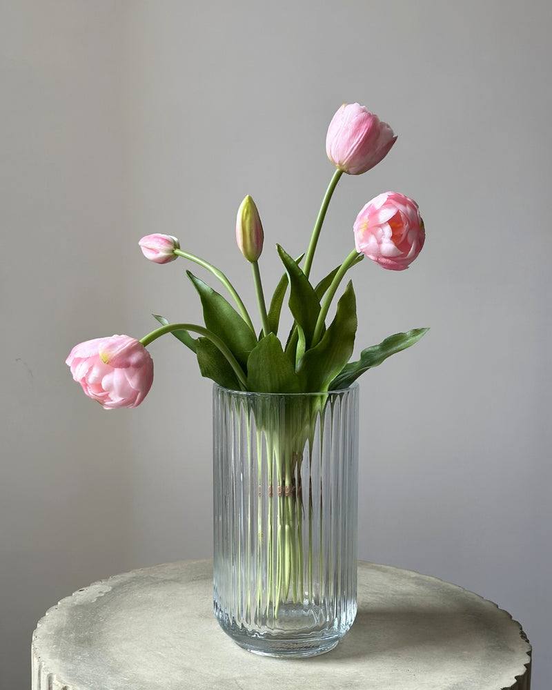 fem lyseroede tulipaner i en glasvase på en cement piedestal