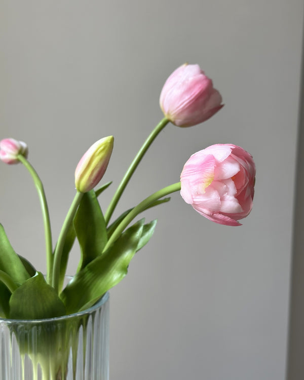 fem lyseroede tulipaner i en glasvase på en cement piedestal
