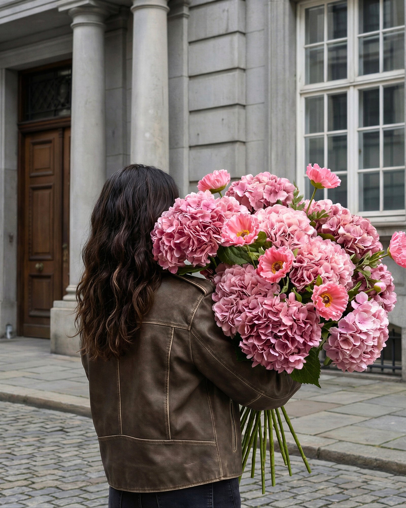 Kvinde bærer stor buket lyserøde realistiske kunstige blomster fra Bloomgaard i bymiljø