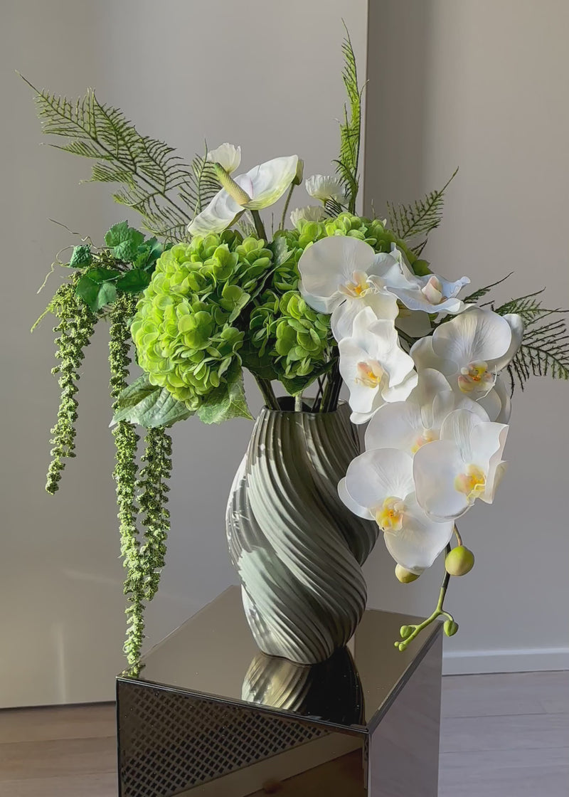En elegant evighedsbuket i klare hvide og grønne nuancer, hvor den smukke orkidé får lov at træde i karakter med sit yndefulde udtryk. De fine, silkebløde kronblade er udformet med stor omhu og føles næsten som en ægte blomst. Kombinationen af lyse toner og friske grønne elementer skaber et roligt, sofistikeret udtryk – perfekt til dig, der elsker et let og eksklusivt look i hjemmet.
Både tidløs og moderne på én gang.