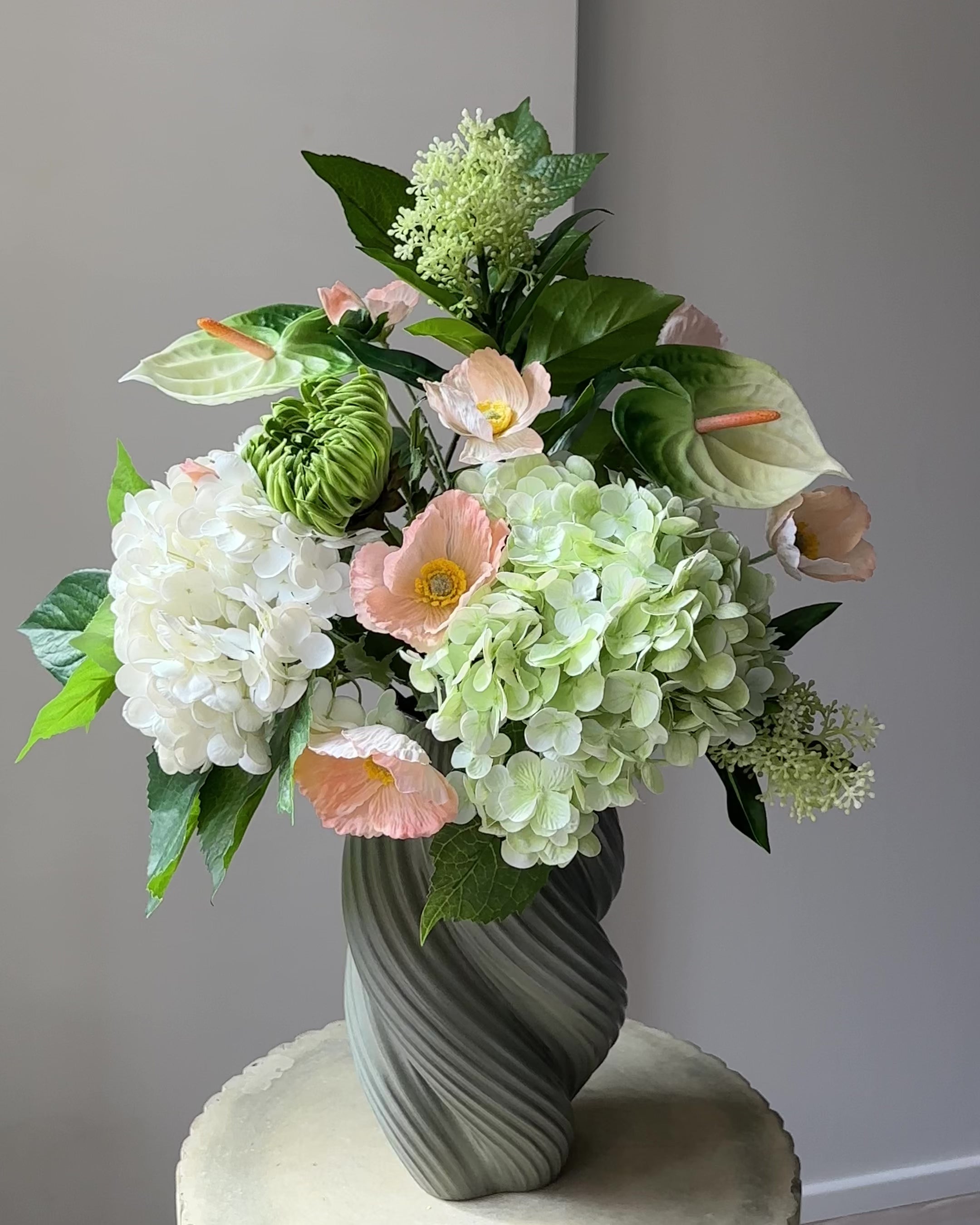 Load video: Blush Pavilion artificial bouquet with white and green hydrangeas, peach poppies, green anthurium and a green cactus dahlia bud in a grey-green twisted vase