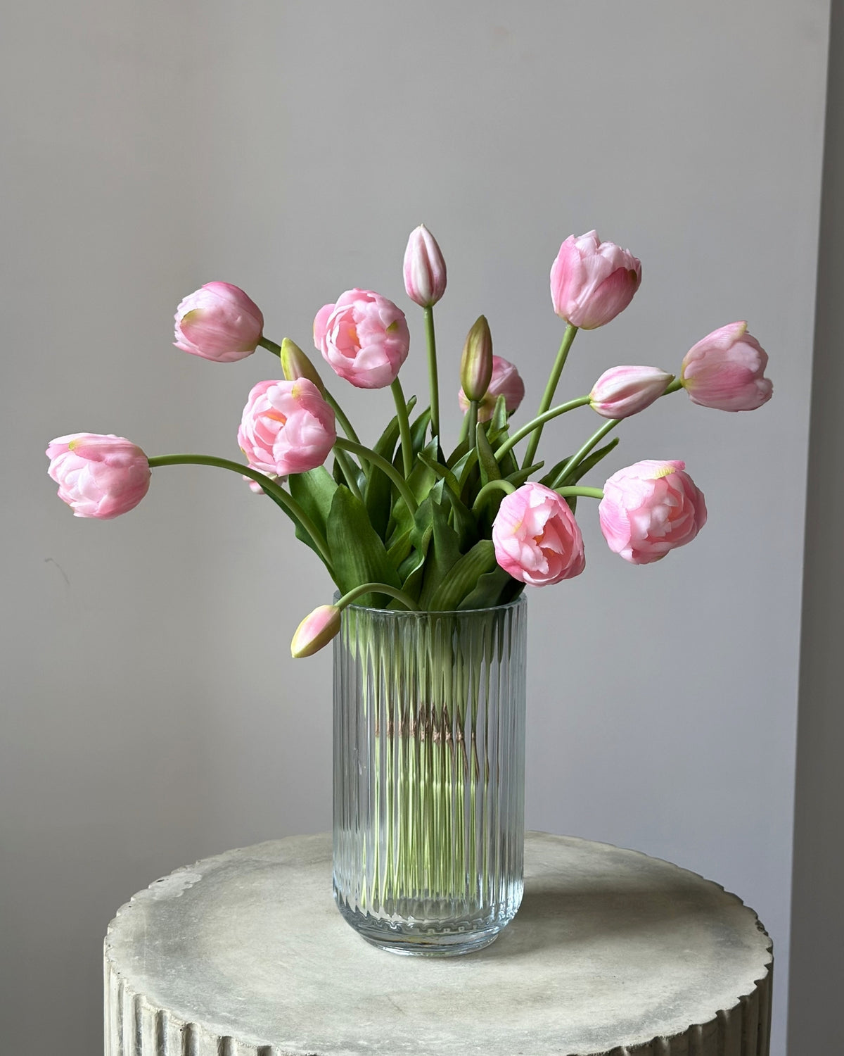 mange kunstige, lyseroede tulipaner i en glasvase på en cement piedestal