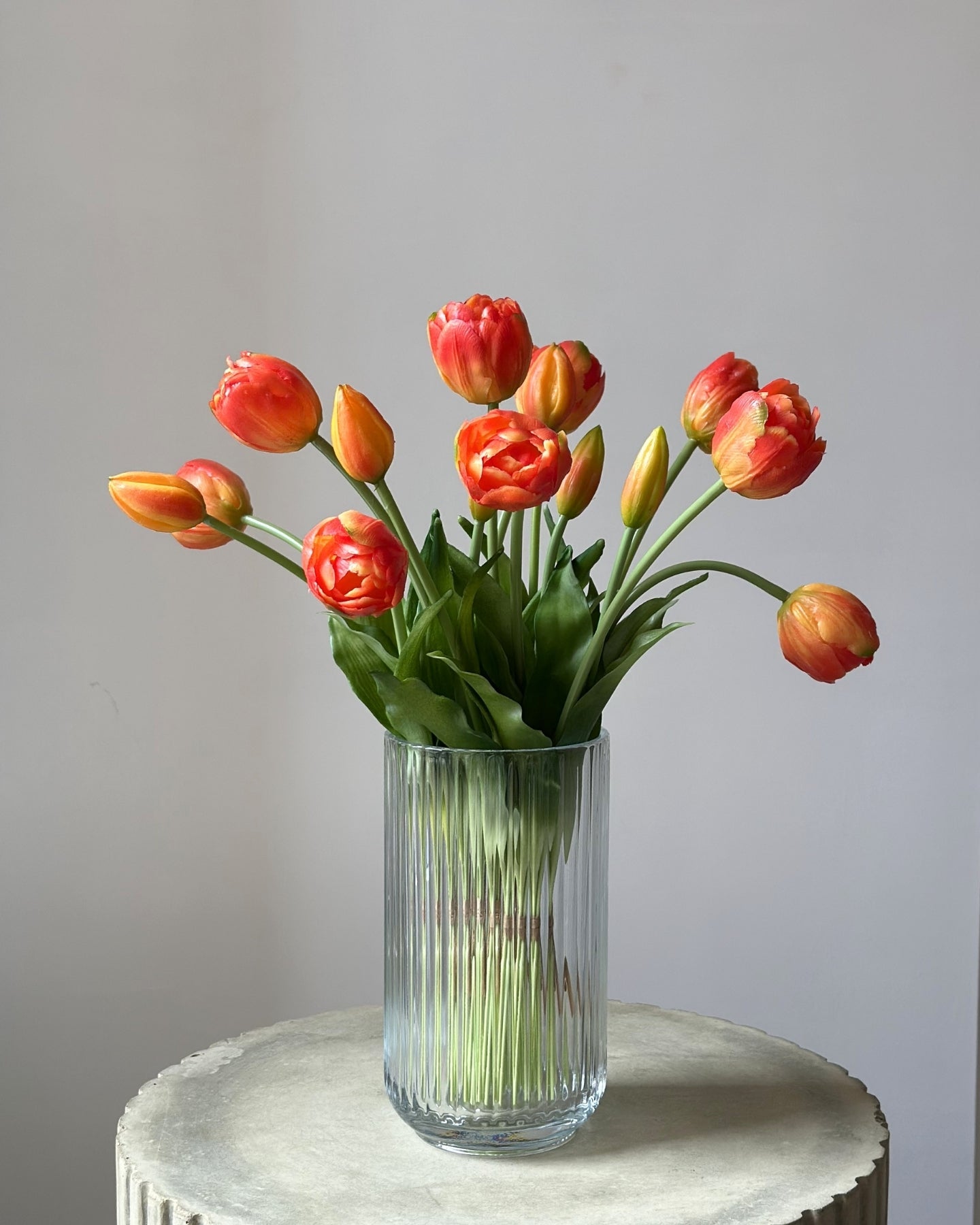 Mange, orange tulipaner i en glasvase på en cementpiedestal