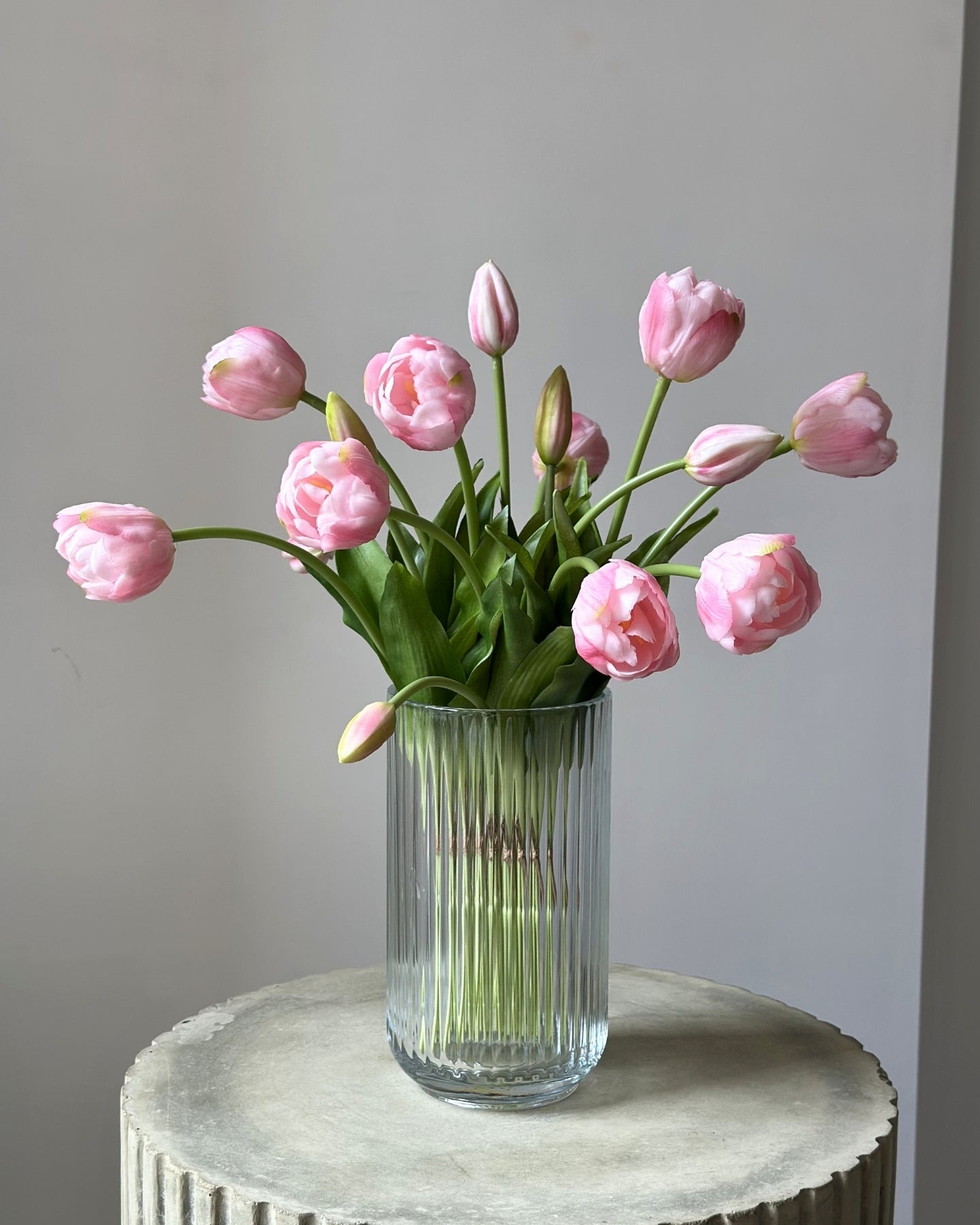 mange kunstige, lyseroede tulipaner i en glasvase på en cement piedestal