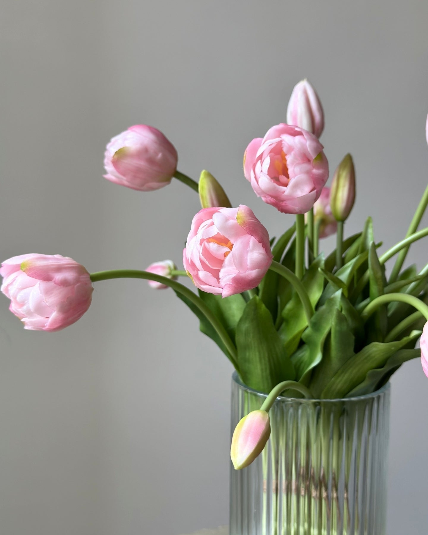 mange kunstige, lyseroede tulipaner i en glasvase på en cement piedestal
