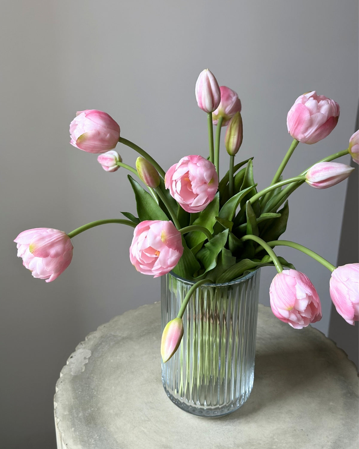 mange kunstige, lyseroede tulipaner i en glasvase på en cement piedestal