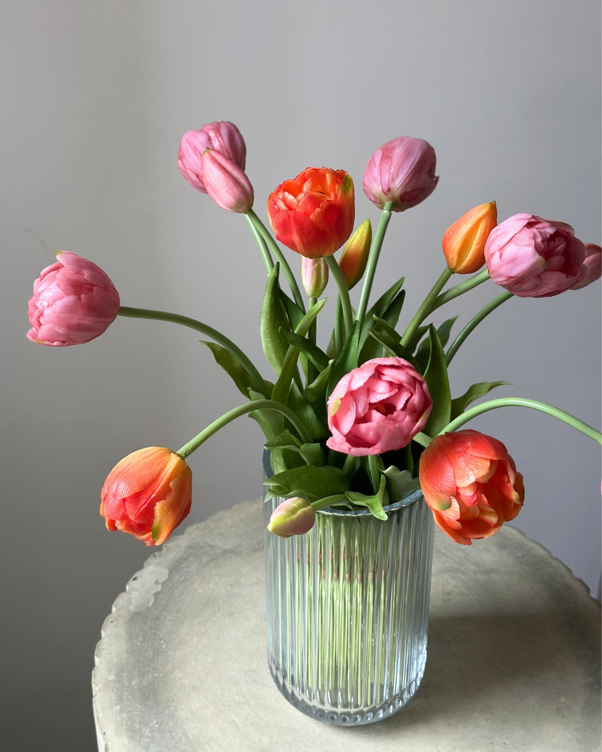Mange lyseroede og orange tulipaner i en glasvase på en cementpiedestal