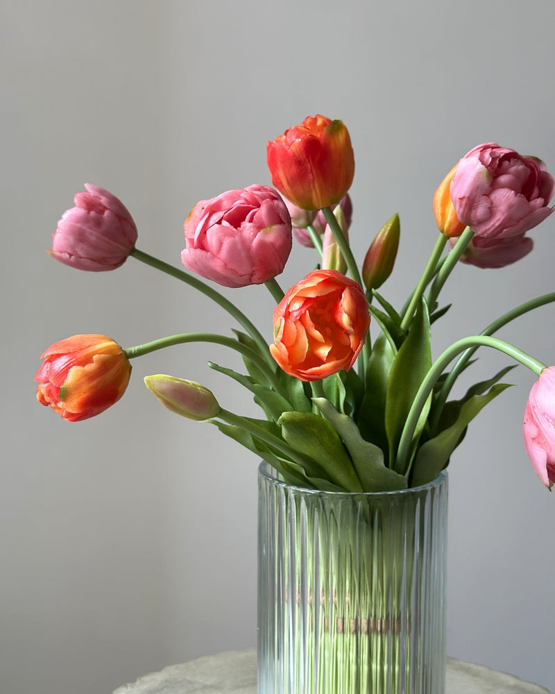 Mange lyseroede og orange tulipaner i en glasvase på en cementpiedestal
