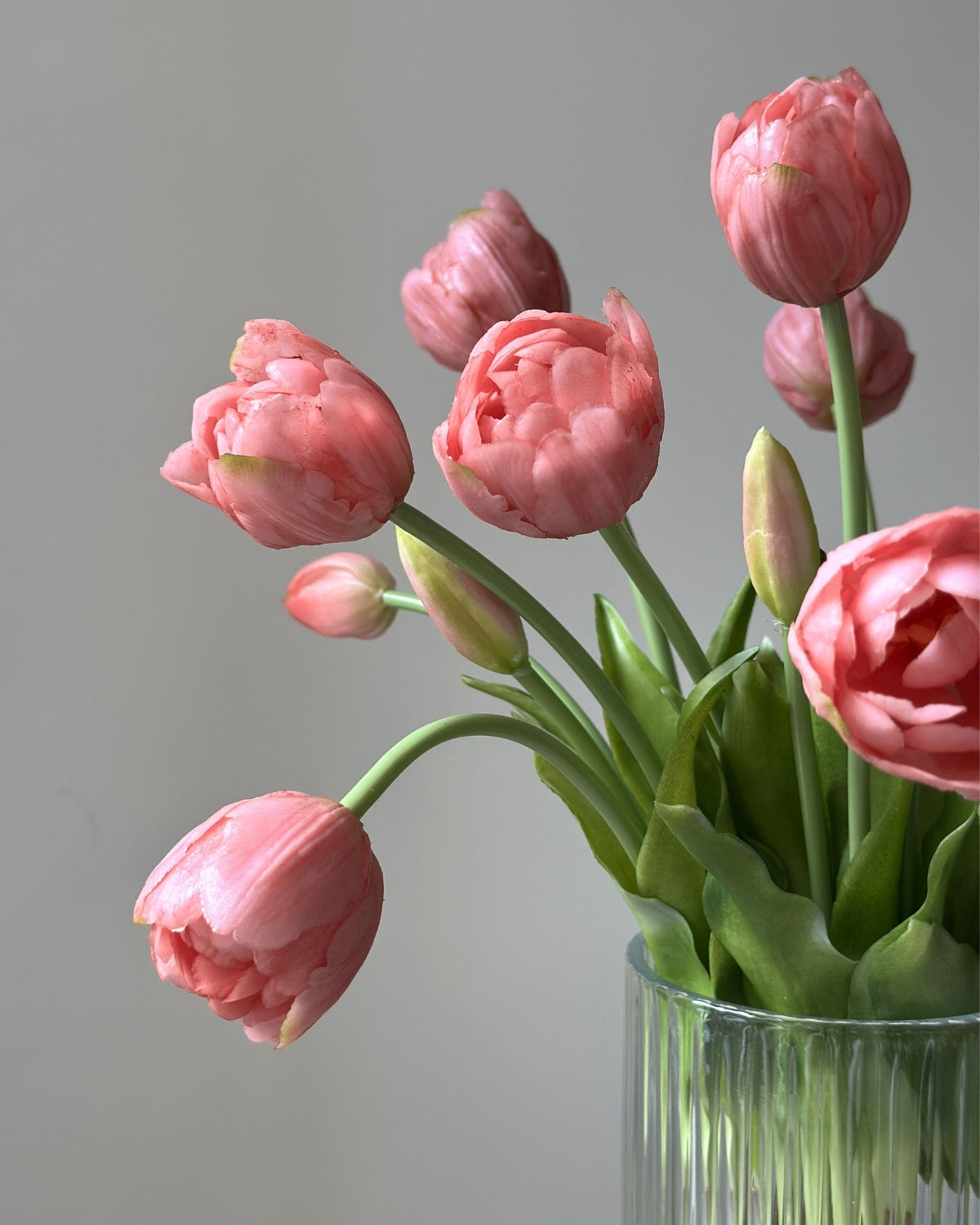 Mange lyseroede tulipaner i en glasvase på en cement piedestal