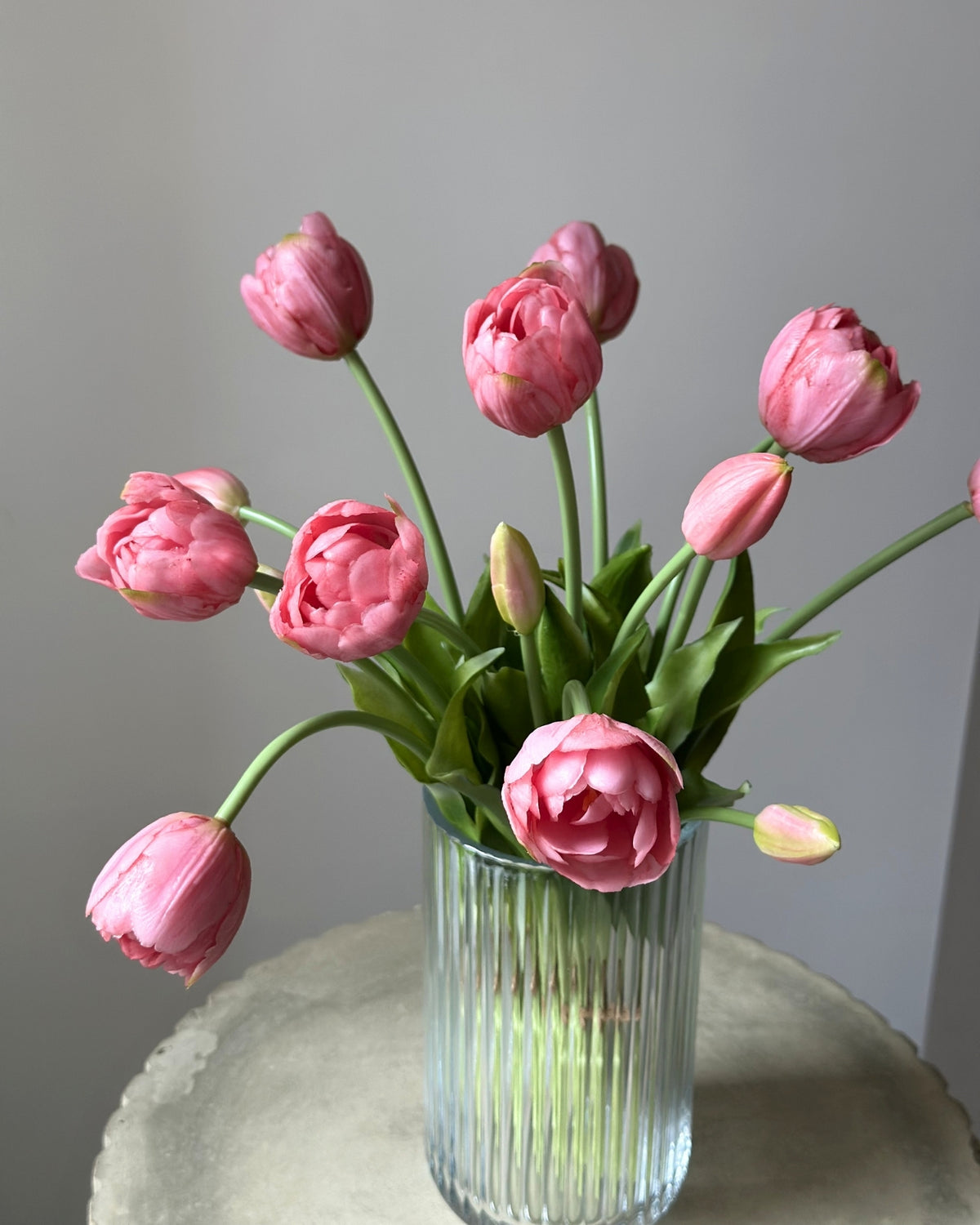 Mange lyseroede tulipaner i en glasvase på en cement piedestal