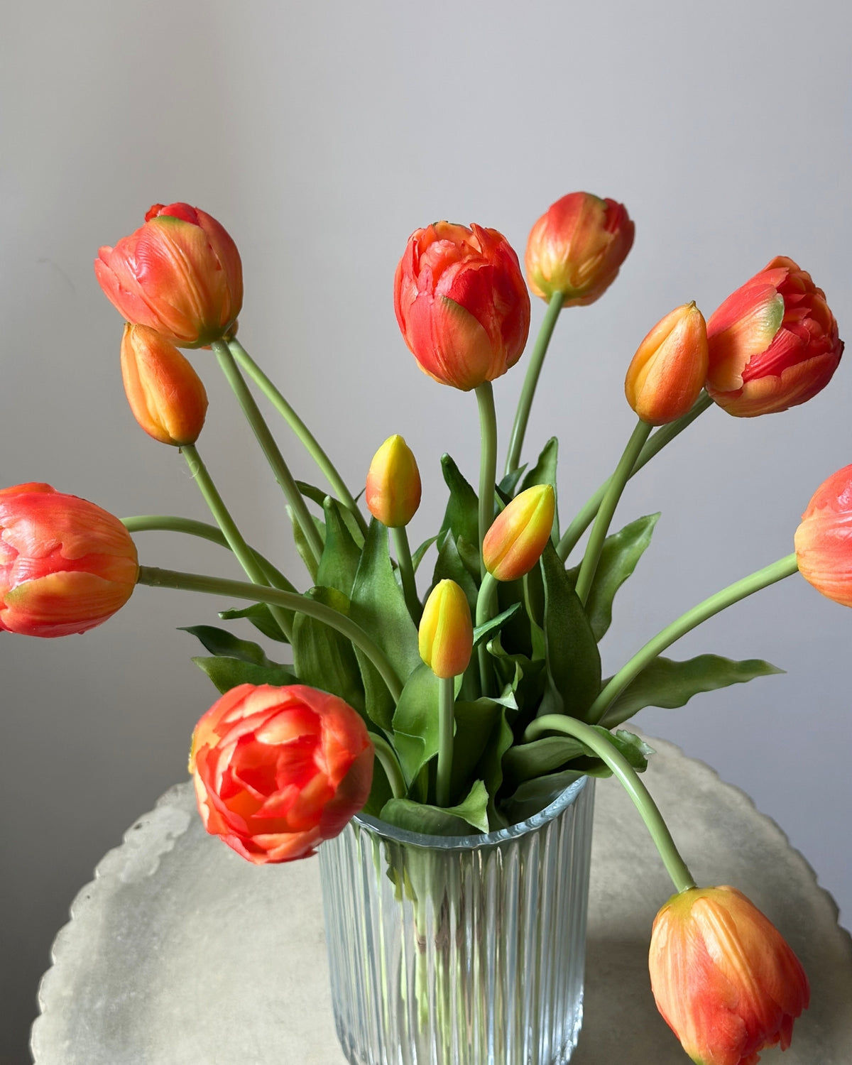 Mange, orange tulipaner i en glasvase på en cementpiedestal